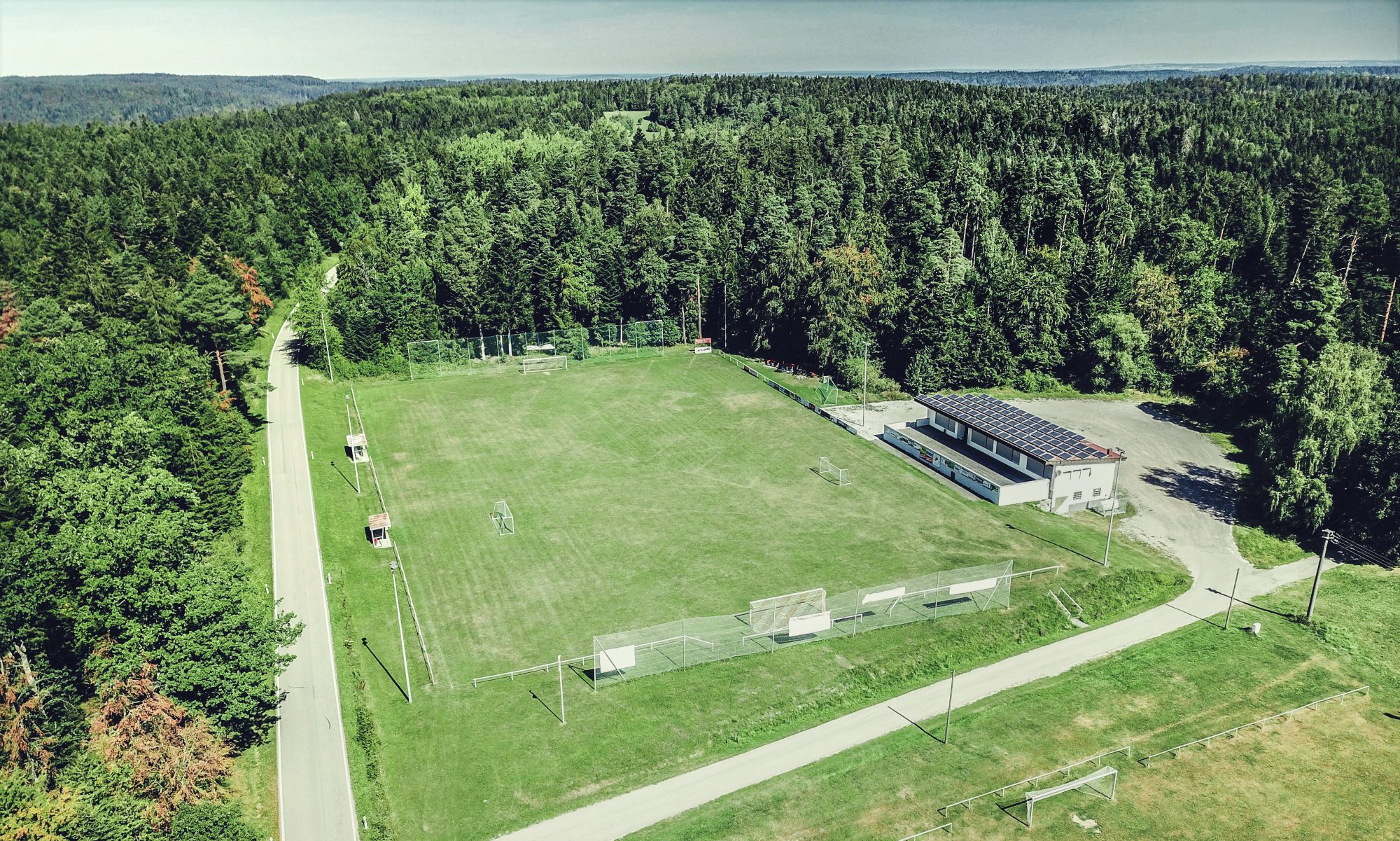 Luftbild des Sportgeländes Reutewasen: der Rasenplatz und das Sportheim, umgeben von Wald